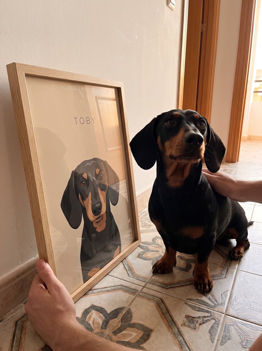 Un perro en el recibidor junto a su retrato sobre fondo arena